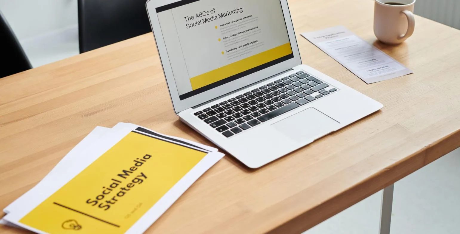 Laptop and printed social media strategy documents on a wooden desk