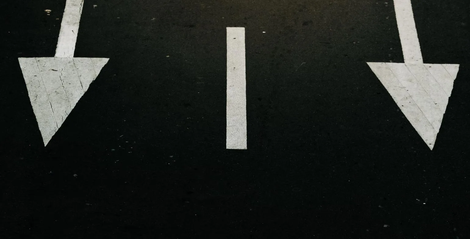 Two white arrows painted on dark asphalt pointing in diverging directions