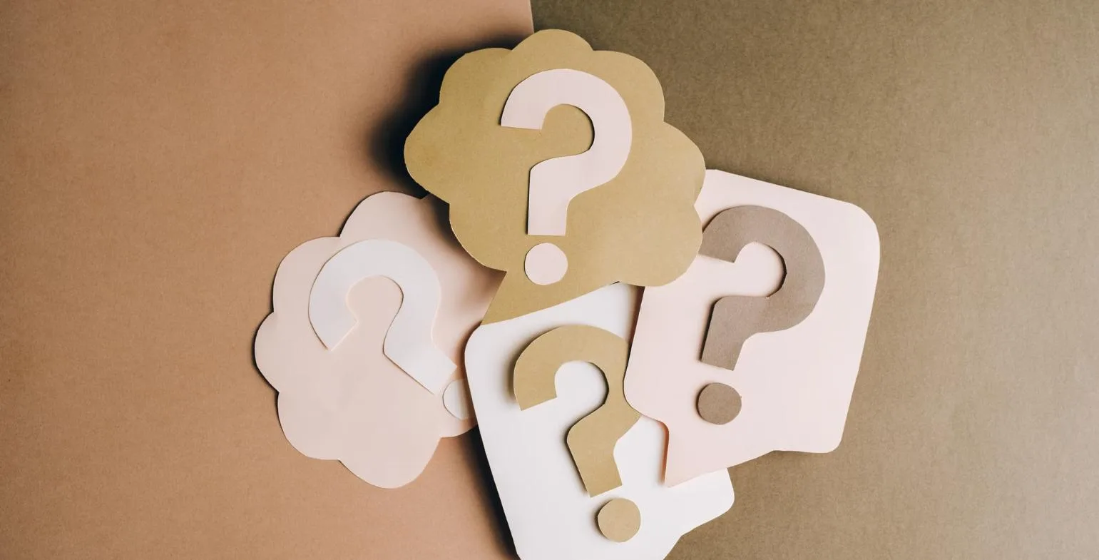 Paper speech bubbles cut into question mark shapes on a two-tone background