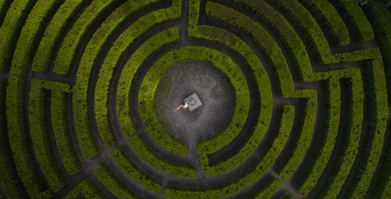Aerial view of a circular hedge maze with a person standing at its centre