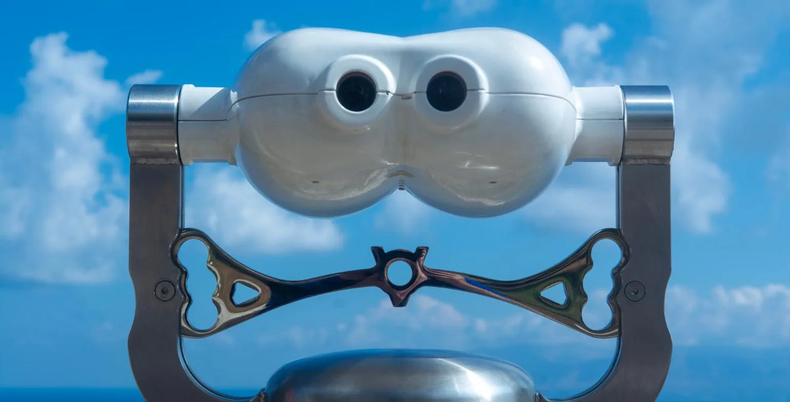 Coin-operated viewing binoculars pointed at the sea under a bright blue sky