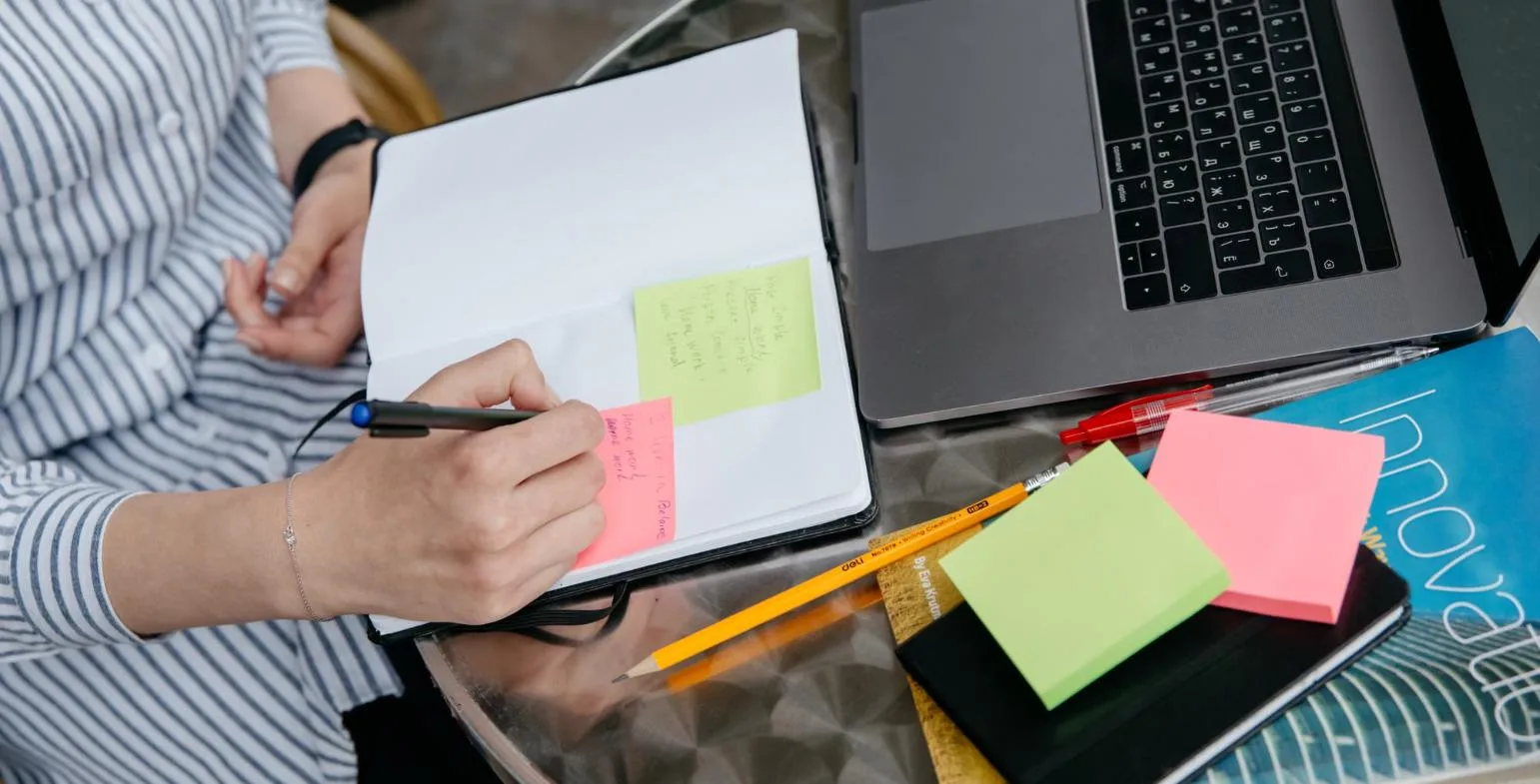 Hand writing notes on colourful sticky notes next to a laptop