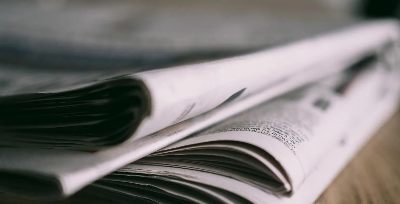 Close-up of folded newspapers stacked on a desk, representing press releases and digital PR
