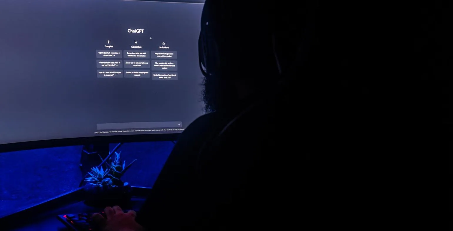 Person working at a curved monitor showing the ChatGPT start screen in a dark room