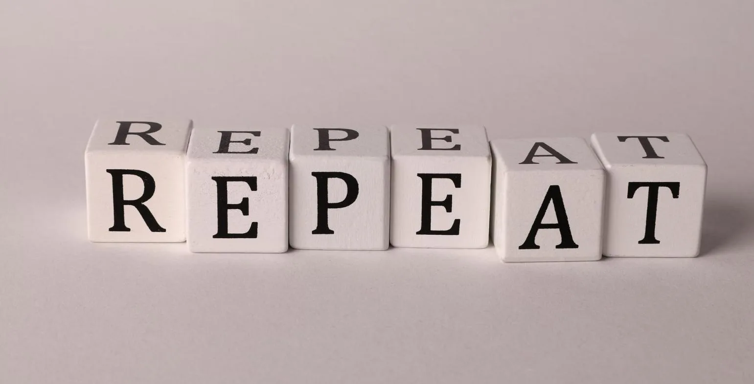 Wooden dice blocks spelling REPEAT on a plain background