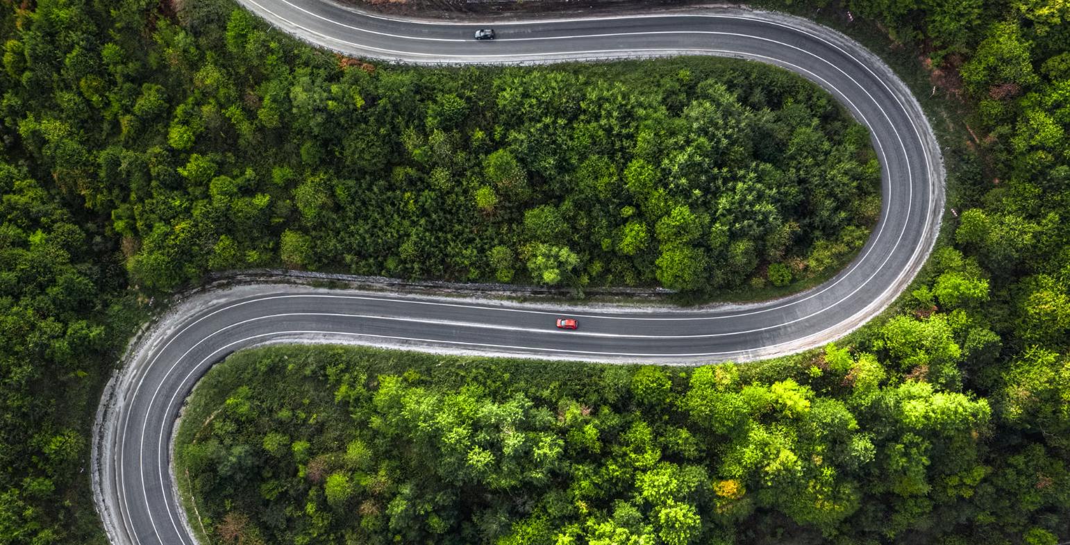 Aerial view of a long winding road curving through a green forest