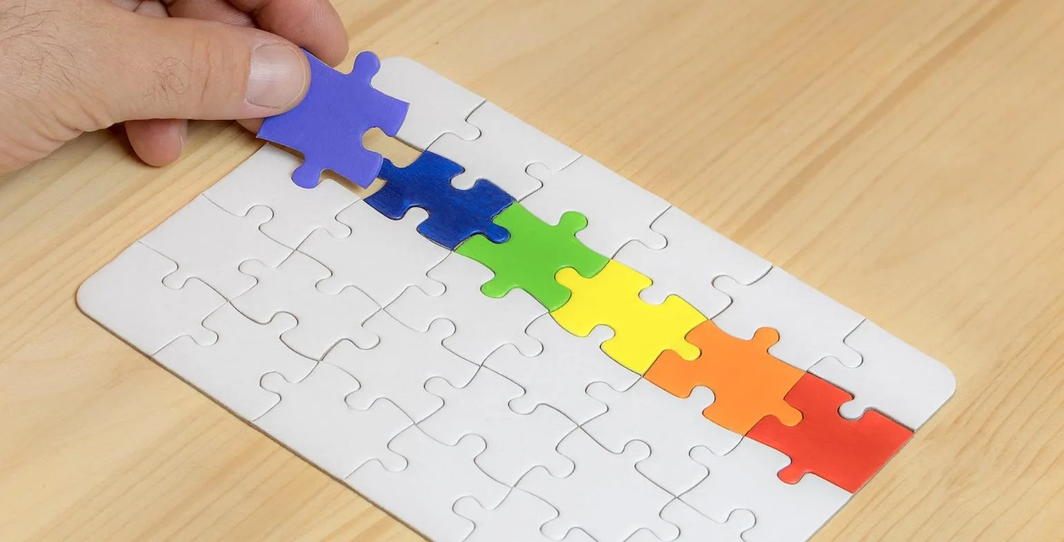 Hand placing a colourful puzzle piece into a jigsaw puzzle