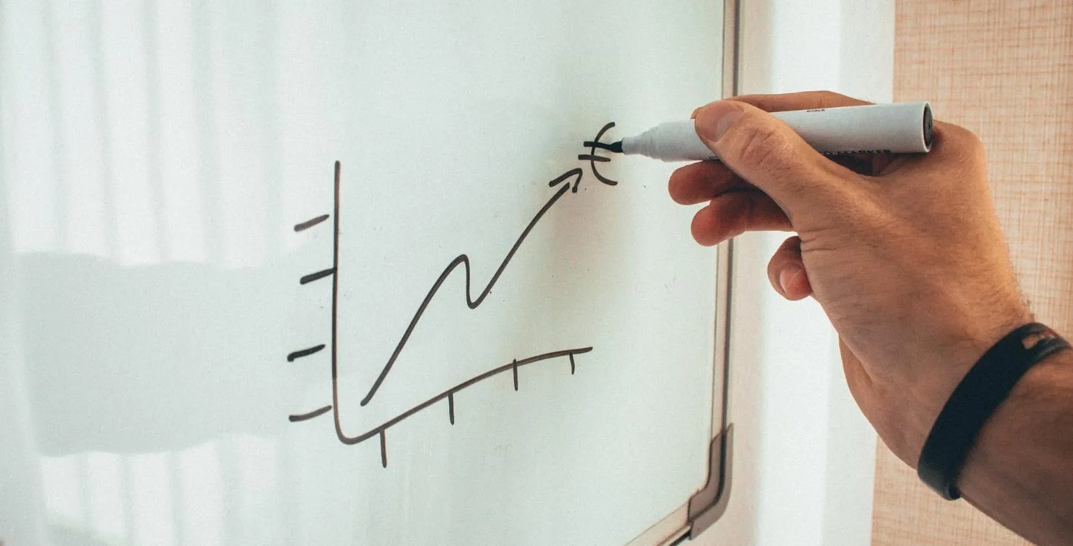 Hand drawing a rising line graph with an upward arrow on a whiteboard