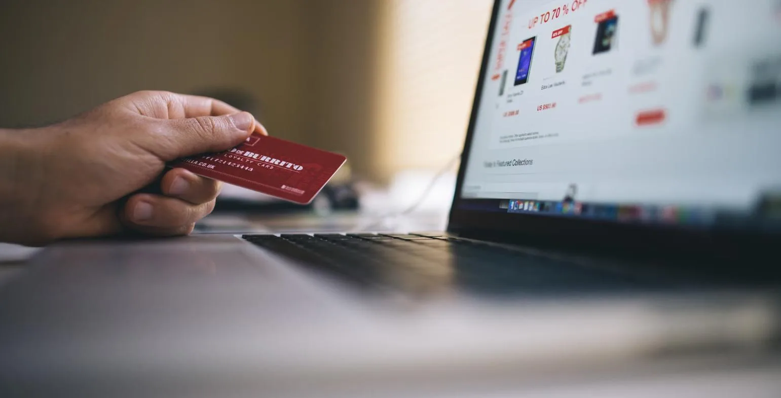 Person holding a payment card in front of an online store on a laptop