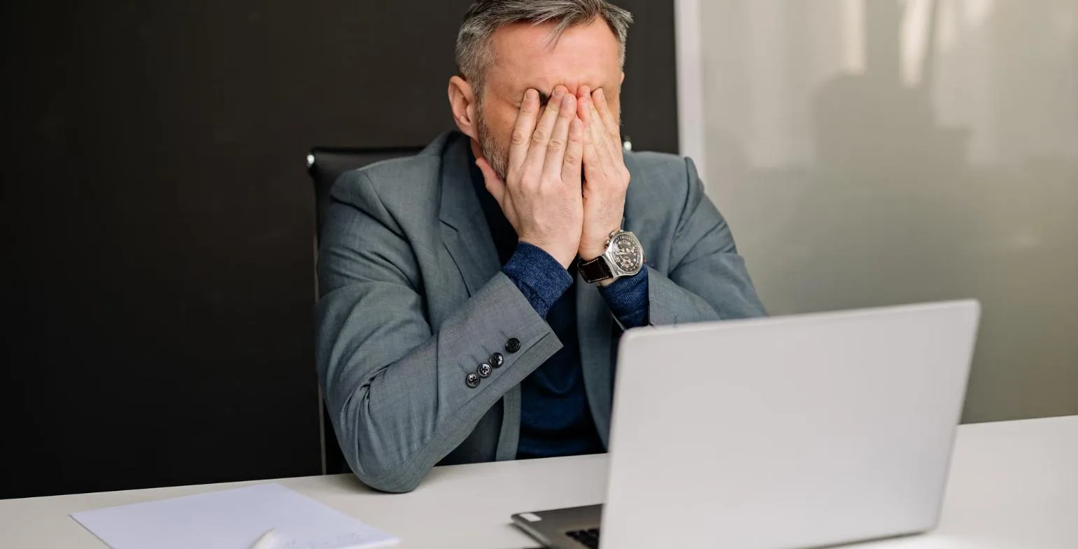 Businessman covering his face in front of a laptop after a drop in performance