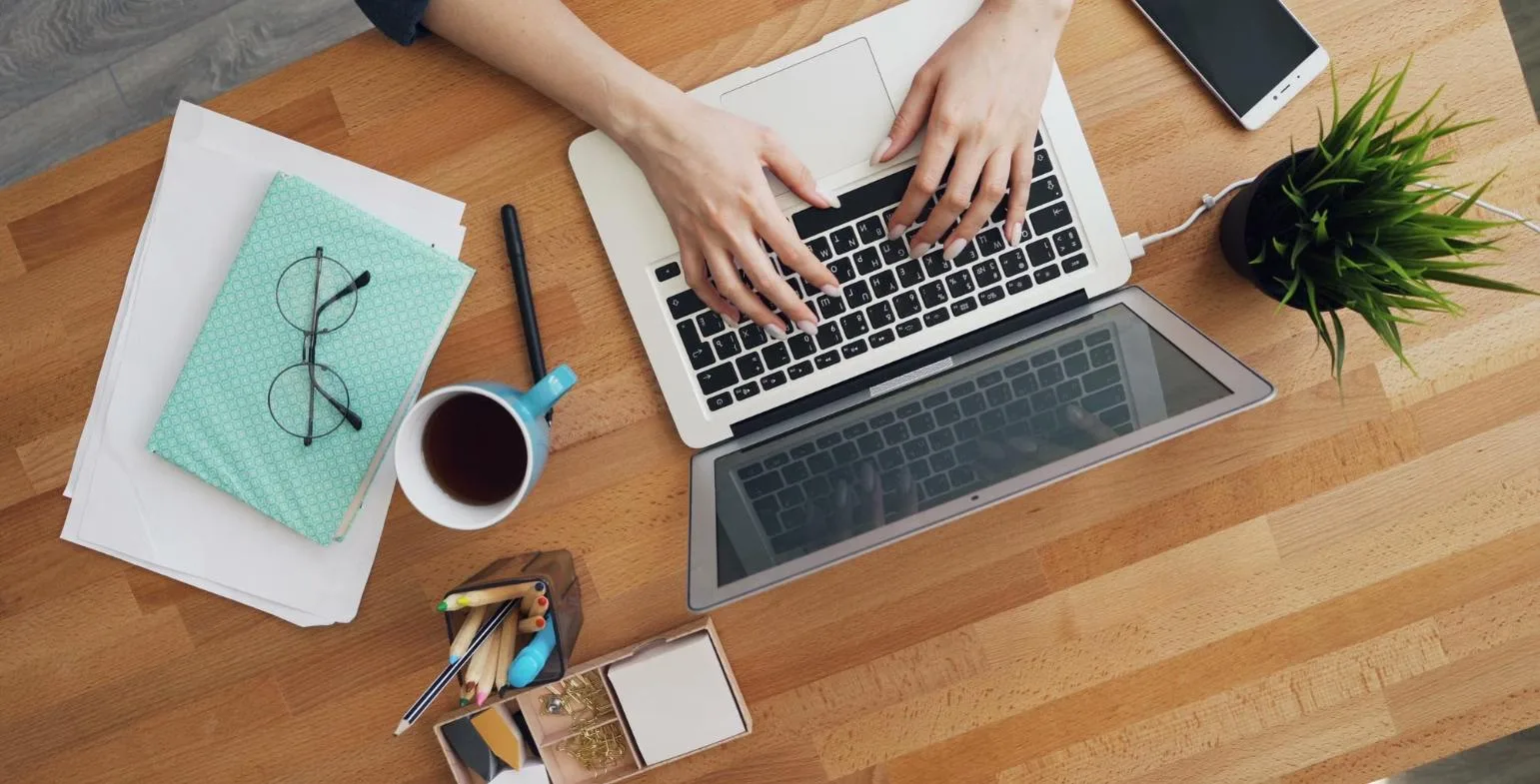 Overhead view of a writer typing a guest post on a laptop at a wooden desk