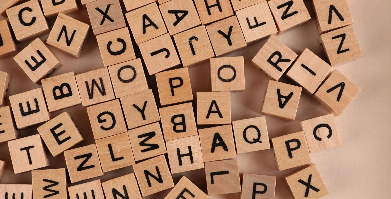 Scattered wooden letter tiles covering a surface, representing language models