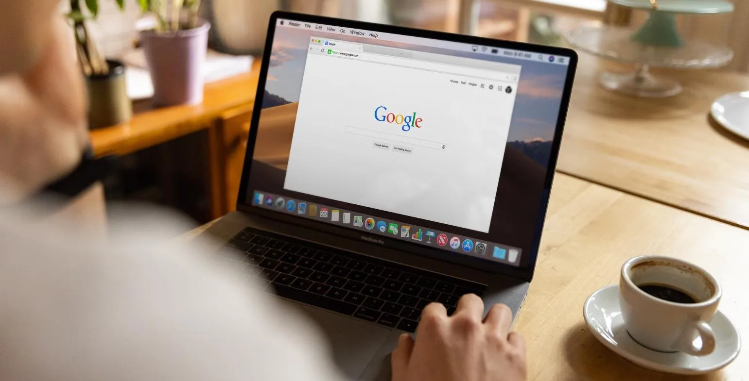 Person browsing the Google homepage on a laptop next to a cup of coffee