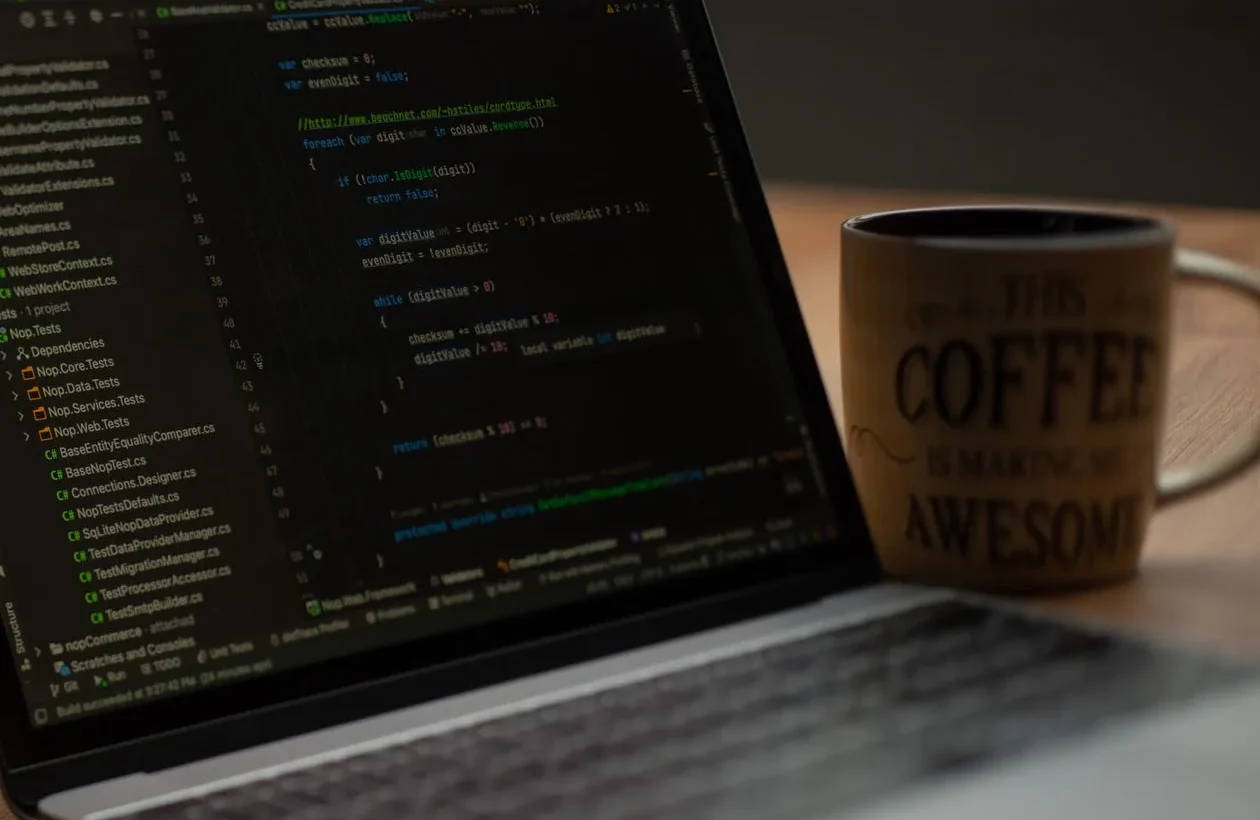 Laptop showing website HTML code being edited, with a coffee mug beside it